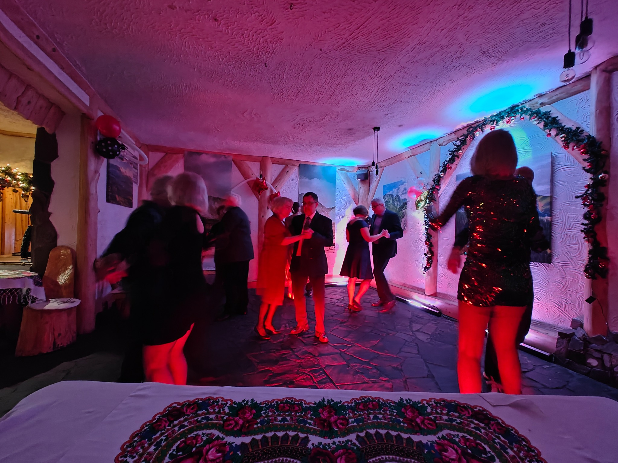 Tańczący goście w sali z dekoracjami świątecznymi i oświetleniem w kolorze różowym i niebieskim.
