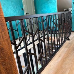 Dawid Kubasa - Nowoczesna, czarna balustrada schodowa z geometrycznym wzorem, widok z góry, na tle turkusowej ściany i drewnianej podłogi. Nietypowy design i kolorystyka.