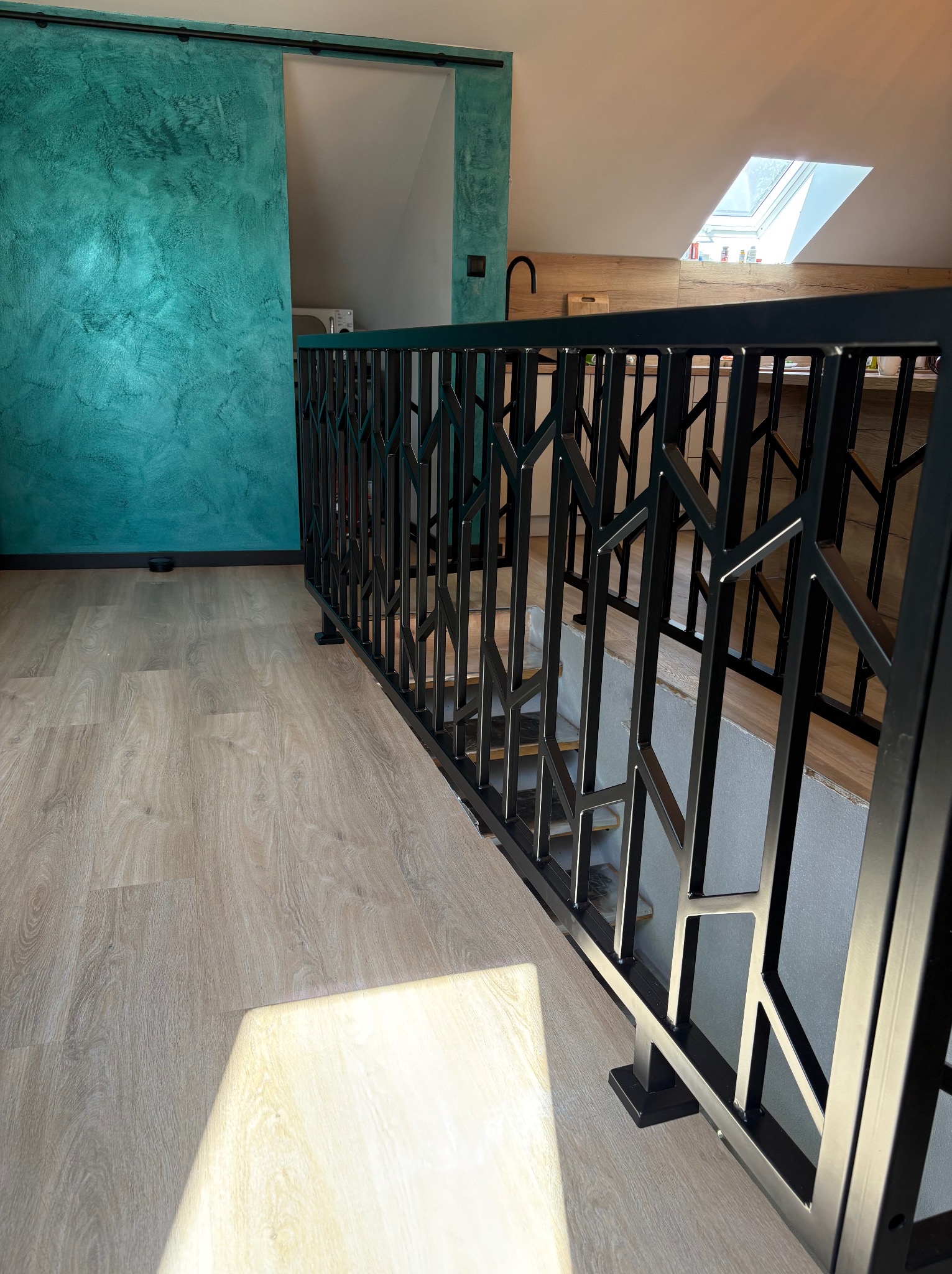 Czarna, metalowa balustrada schodowa o geometrycznym wzorze w nowoczesnym wnętrzu. Widok na schody i turkusową ścianę z przesuwnymi drzwiami.