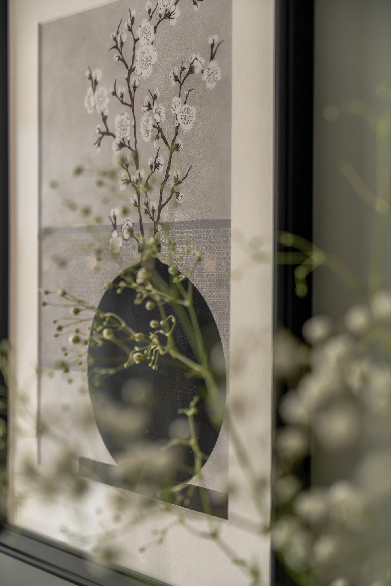 Grafika w ramie z motywem kwiatowym, częściowo zasłonięta przez bukiet gipsówki. Stonowana kolorystyka, nowoczesny design, element dekoracyjny wnętrza.