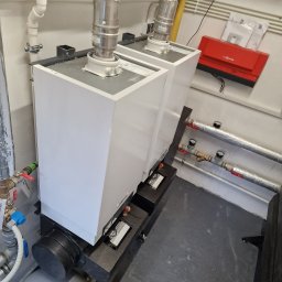 PPHU MUFA - Dwa białe kotły grzewcze z podłączonymi rurami spalinowymi i instalacją hydrauliczną, widoczny czerwony moduł sterujący Viessmann na ścianie.