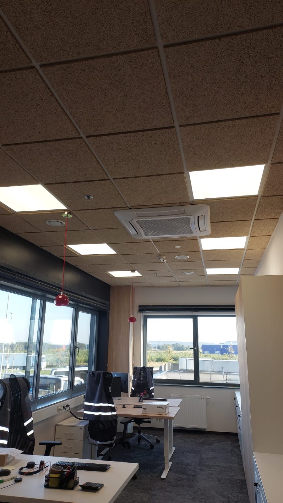 Biuro z podwieszanym sufitem z płyt akustycznych, klimatyzacją kasetonową i oświetleniem LED, widok z perspektywy osoby stojącej w pomieszczeniu.