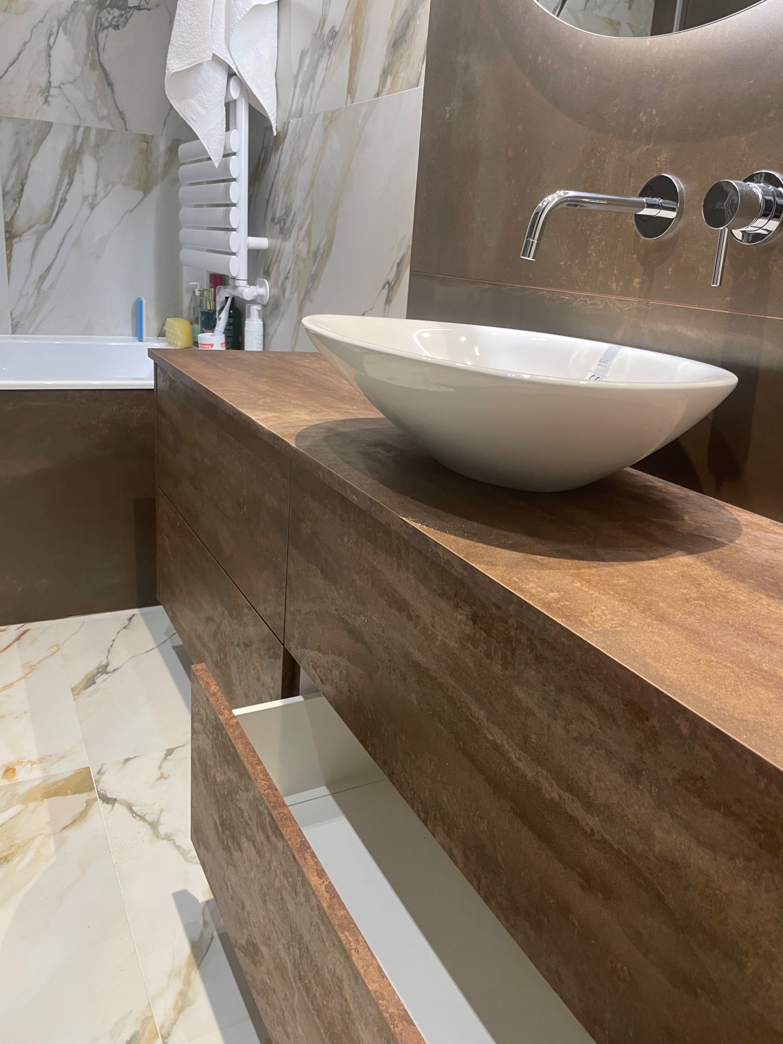 Nowoczesna łazienka z brązową szafką pod umywalkę, białą umywalką nablatową i otwartą szufladą, marmurowe płytki na ścianach i podłodze.
