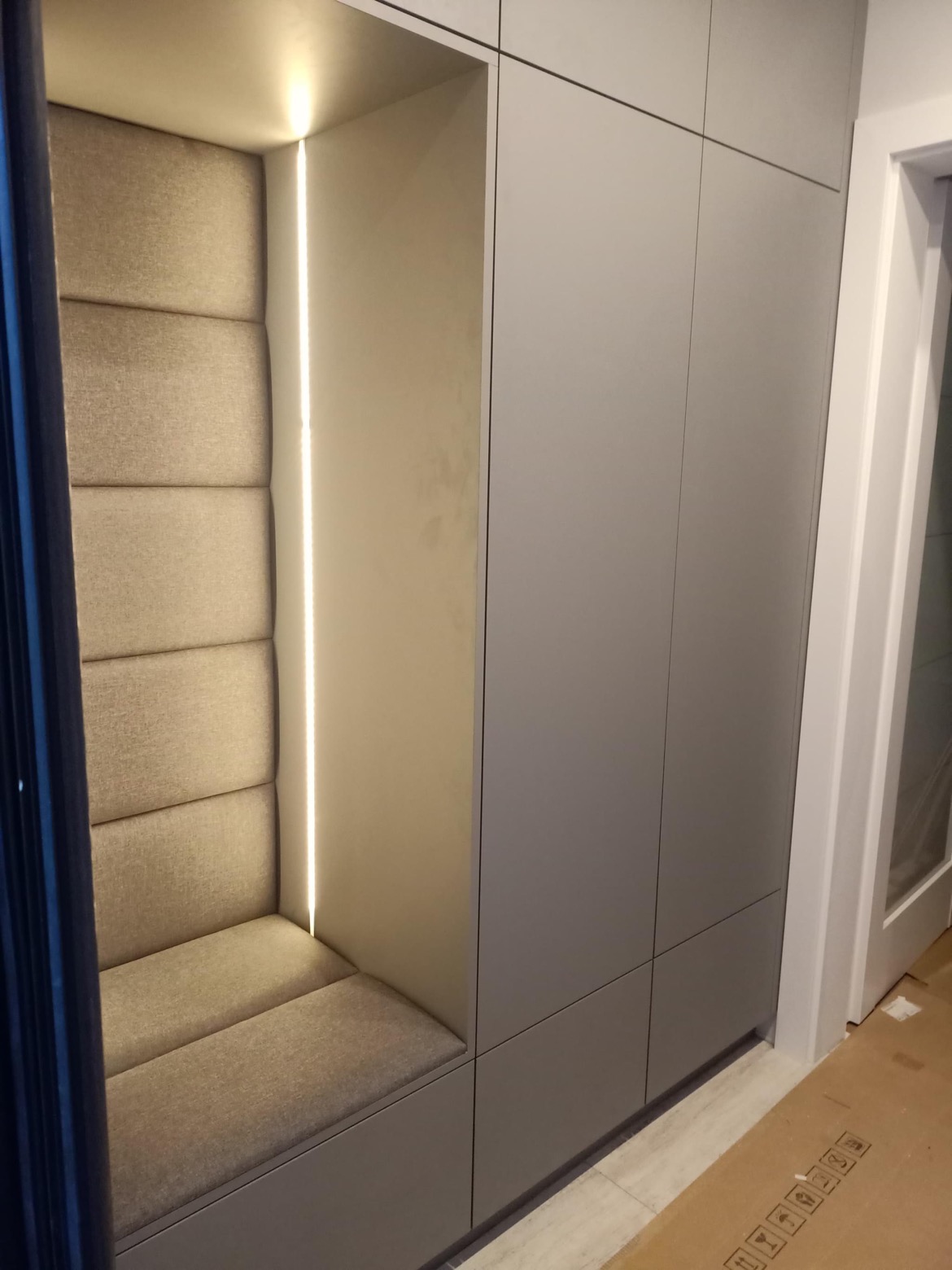 Szara szafa wnękowa z siedziskiem i oświetleniem LED w pionowej szczelinie.