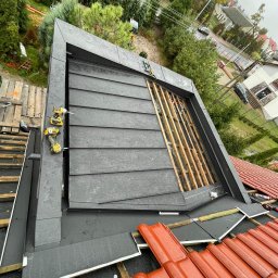 DEKARMAX Jakub Olbryś - Montaż obróbek blacharskich na dachu z widoczną więźbą i narzędziami, ujęcie z góry w pochmurny dzień.