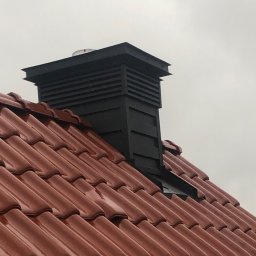 DEKARMAX Jakub Olbryś - Czerwona dachówka ceramiczna z czarnym kominem wentylacyjnym, widok z dołu na tle pochmurnego nieba.