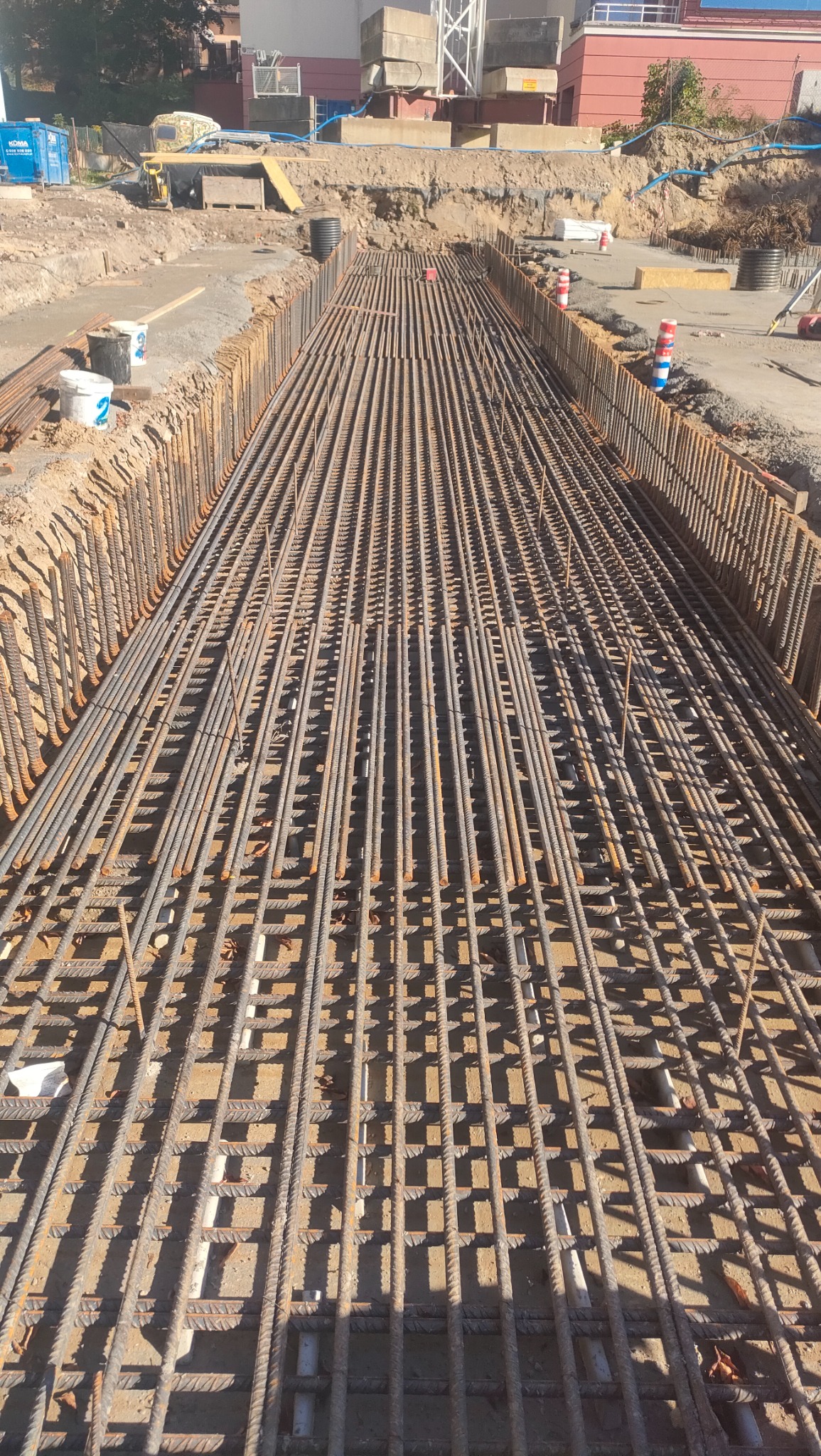 Zbrojenie płyty fundamentowej w wykopie, widok z góry na siatkę z prętów stalowych, przygotowane do zalania betonem.