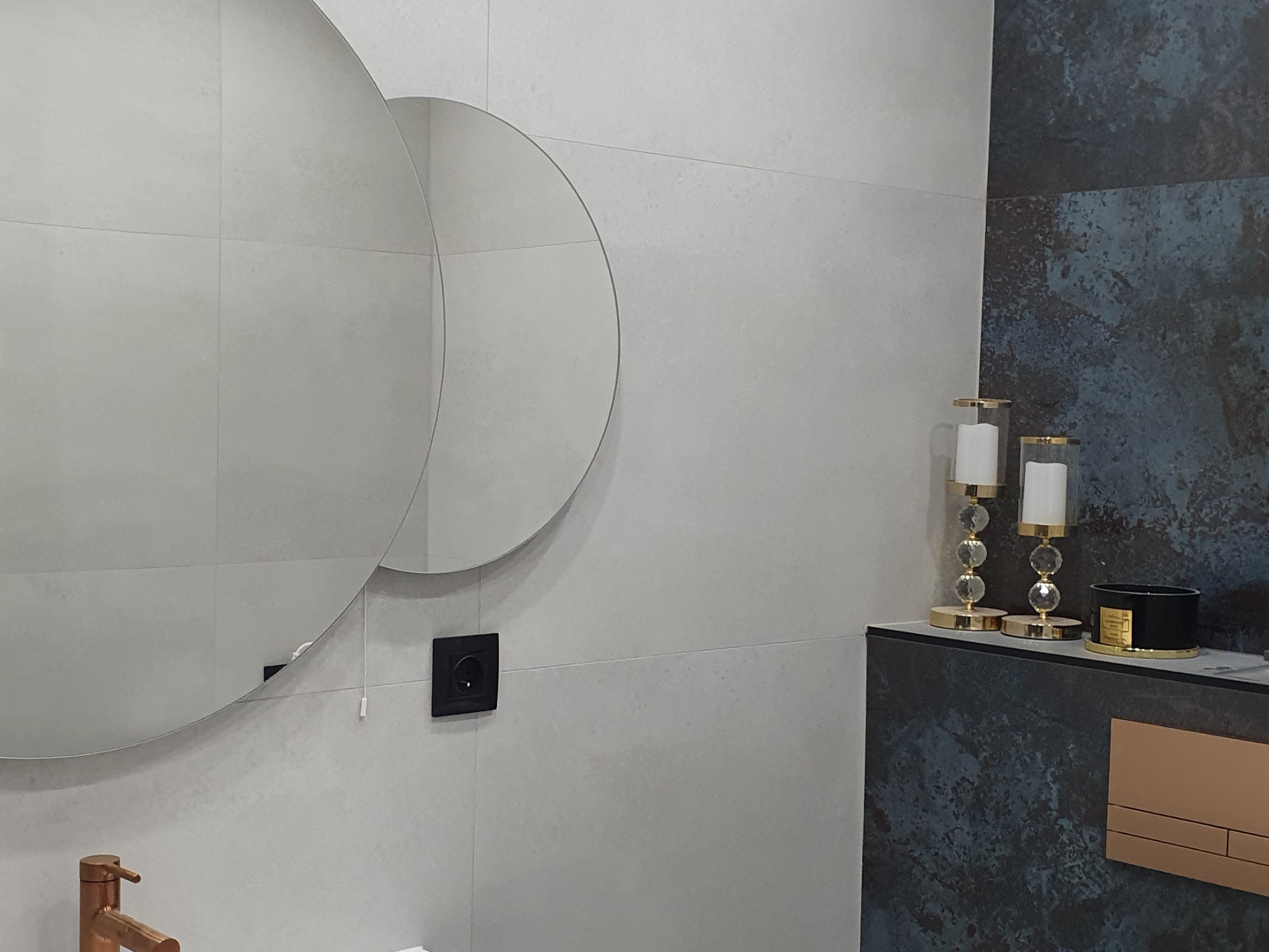 Nowoczesna łazienka z dwoma okrągłymi lustrami, szarymi płytkami ściennymi, dekoracyjnymi świecznikami i czarną armaturą.