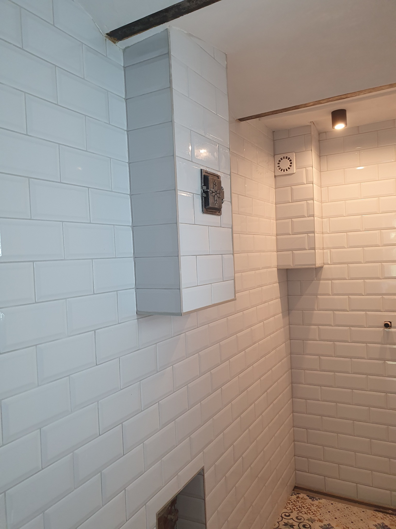 Białe, błyszczące płytki typu metro ułożone w łazience, z widocznym ozdobnym zaworem i fragmentem podłogi. Wykończenie w stylu minimalistycznym.