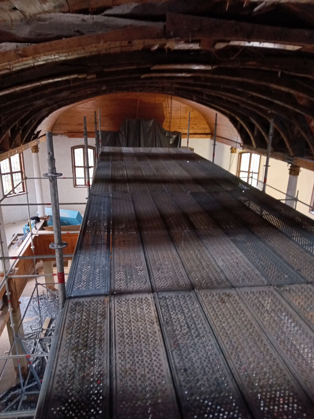 Wnętrze budynku w trakcie renowacji z widocznym rusztowaniem i elementami konstrukcyjnymi sklepienia. Prace remontowe w zabytkowym obiekcie.