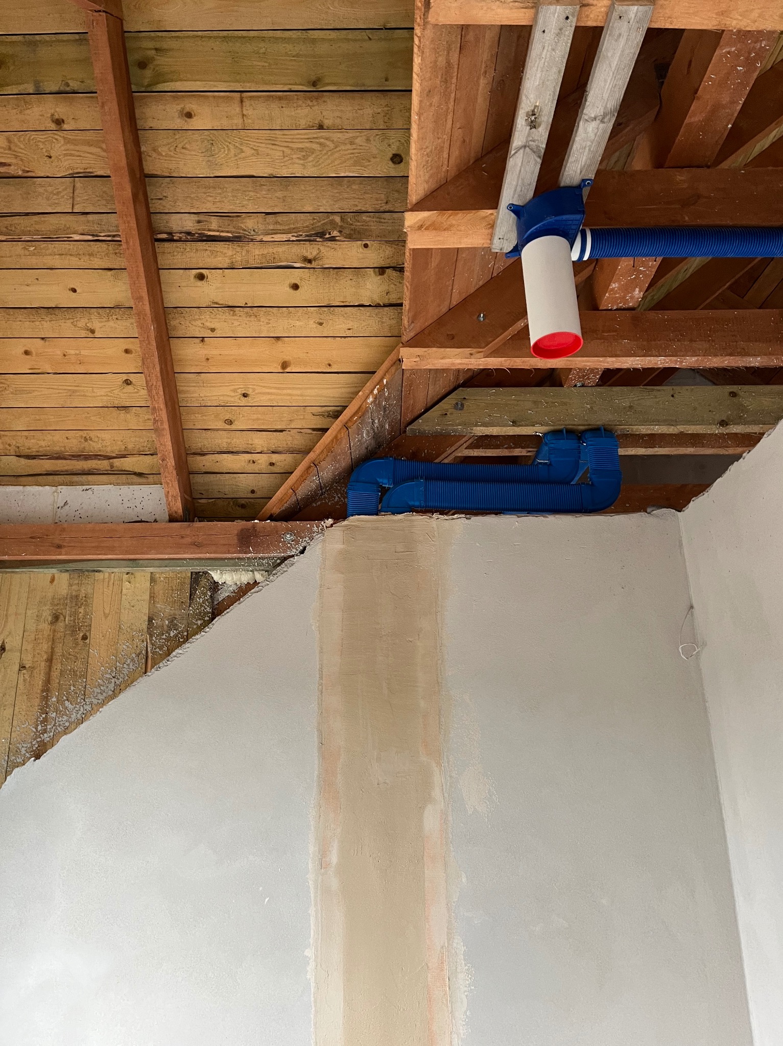 Niebieskie rury wentylacyjne zamontowane pod drewnianym stropem, widoczne elementy instalacji w surowym stanie.