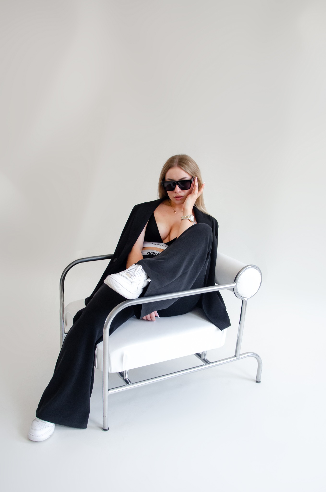 Portret kobiety w czarnym garniturze i okularach przeciwsłonecznych, siedzącej na białym krześle w studio w Częstochowie. Uwagę przyciąga złoty zegarek na jej nadgarstku.