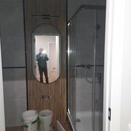 MK RENOV Marek Kondracki - Nowoczesna łazienka w trakcie remontu: kabina prysznicowa z chromowanymi elementami, owalne lustro z podświetleniem, drewniane panele ścienne i widoczne wiadra z farbą.