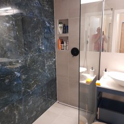 MK RENOV Marek Kondracki - Nowoczesna łazienka po remoncie: kabina typu walk-in z czarną armaturą, ściana wyłożona marmurkowymi płytkami w odcieniach granatu i szarości, wbudowane półki z kosmetykami, umywalki nablatowe...