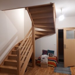 MK RENOV Marek Kondracki - Drewniane schody spiralne z jasnego drewna prowadzące na antresolę w jasnym wnętrzu, widoczne z dołu, z elementami wykończenia pod sufitem.