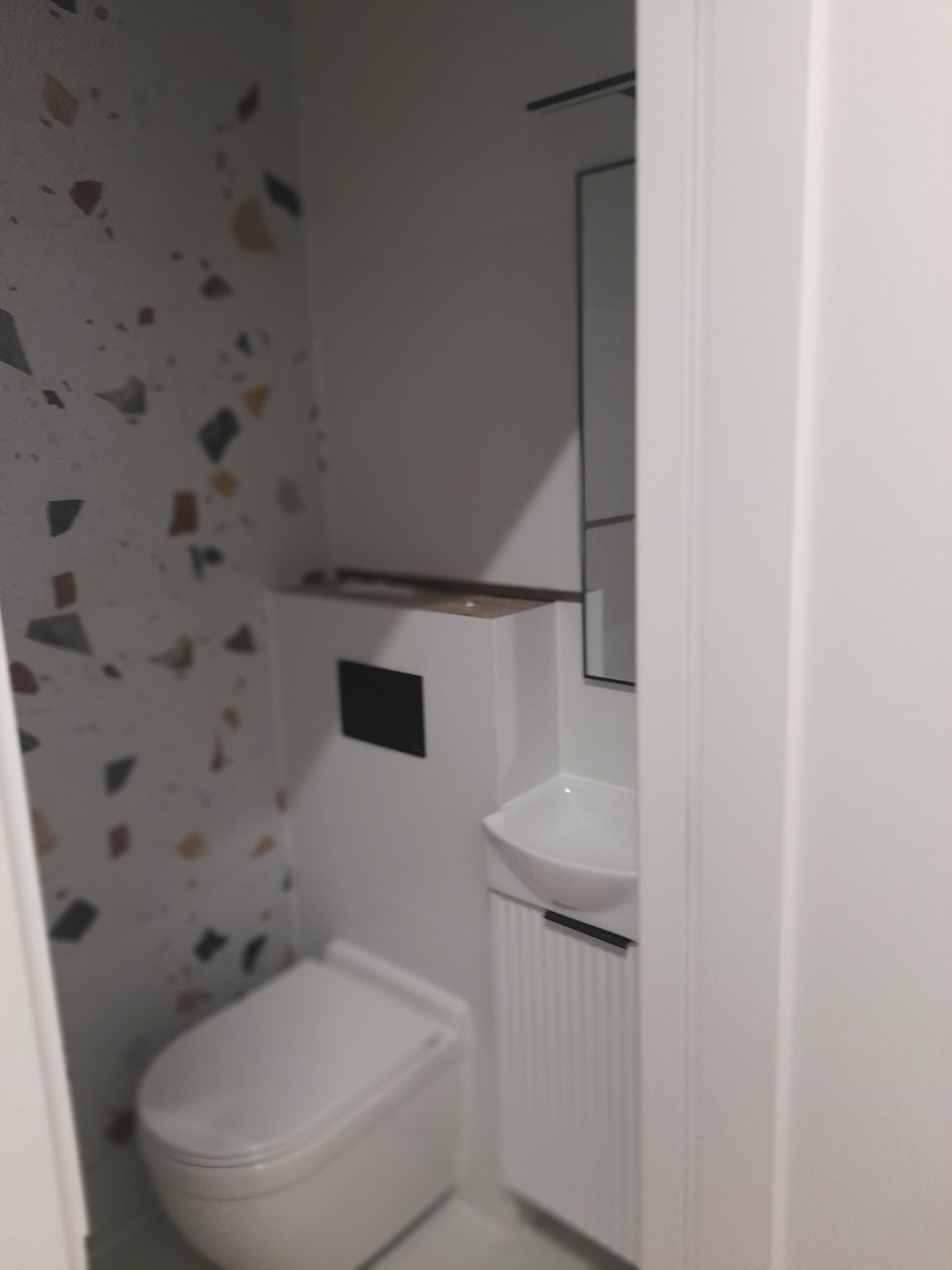 Nowoczesna toaleta z zabudowaną spłuczką, umywalką na szafce z ryflowanym frontem i lustrem, ściana wykończona płytkami imitującymi lastryko.