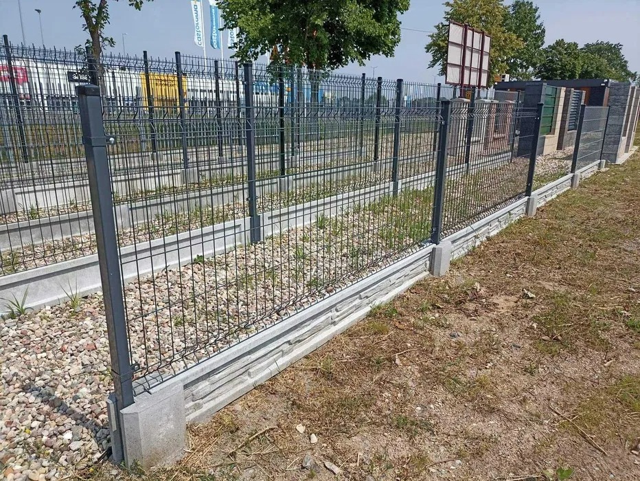 Ogrodzenie panelowe z podmurówką betonową w Makowie Mazowieckim, widok z boku, z fragmentem terenu przed i za ogrodzeniem.