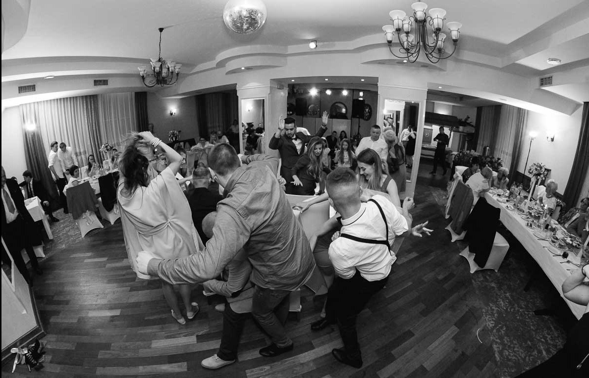 Czarno-białe zdjęcie z wesela w Kielcach, ukazujące gości tańczących na parkiecie, widok z szerokiego kąta z perspektywy żabiej, z dekoracyjną kulą dyskotekową pod sufitem.
