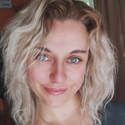 Aleksandra Smmogorzewska - Portret uśmiechniętej kobiety o blond włosach i niebieskich oczach, skierowanej twarzą w stronę obiektywu, z delikatnym makijażem i widoczną srebrną biżuterią.