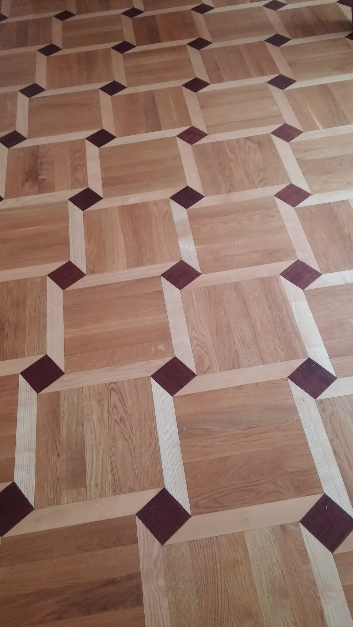 Parkiet ułożony we wzór geometryczny z kwadratów i rombów w odcieniach brązu i beżu.