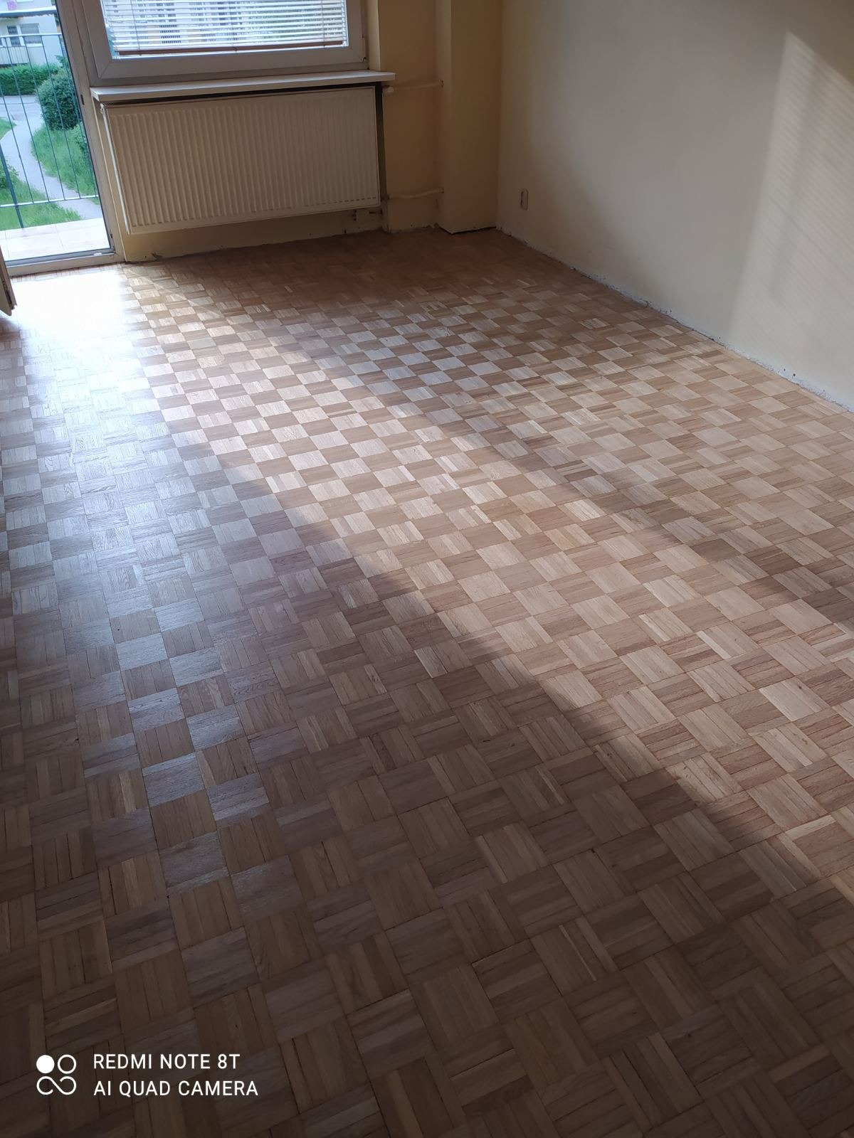 Ułożony parkiet w jodełkę w jasnym pokoju z grzejnikiem w Gdańsku, widoczne niedoskonałości przy ścianach.