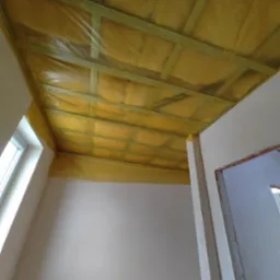 Izolacja termiczna poddasza z widoczną folią paroizolacyjną i drewnianą konstrukcją szkieletową, ściany przygotowane do dalszych prac wykończeniowych.