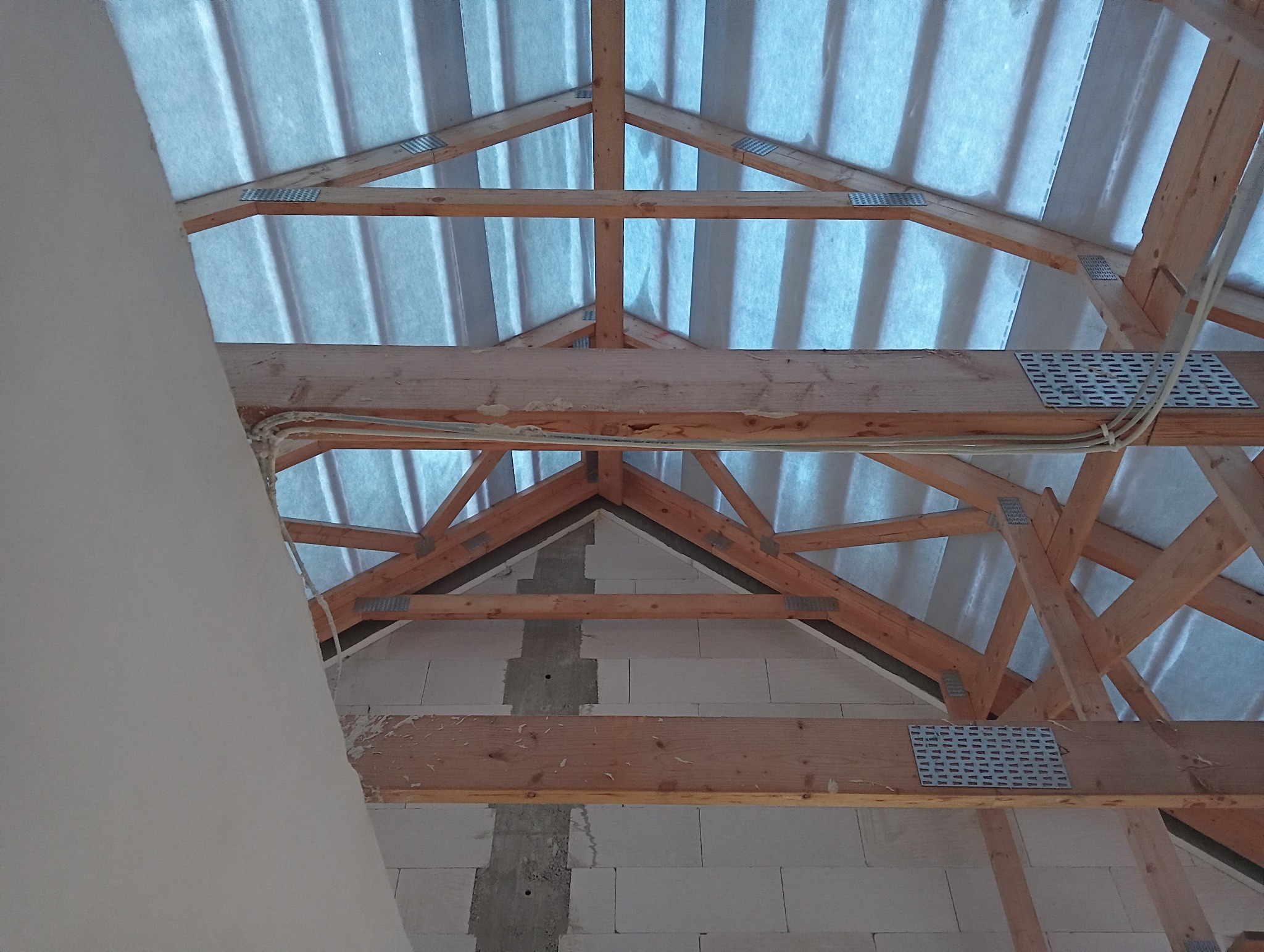 Konstrukcja drewniana dachu z widocznymi elementami mocującymi, izolacją i fragmentem ściany z betonu komórkowego, widok od wewnątrz podczas prac remontowych.