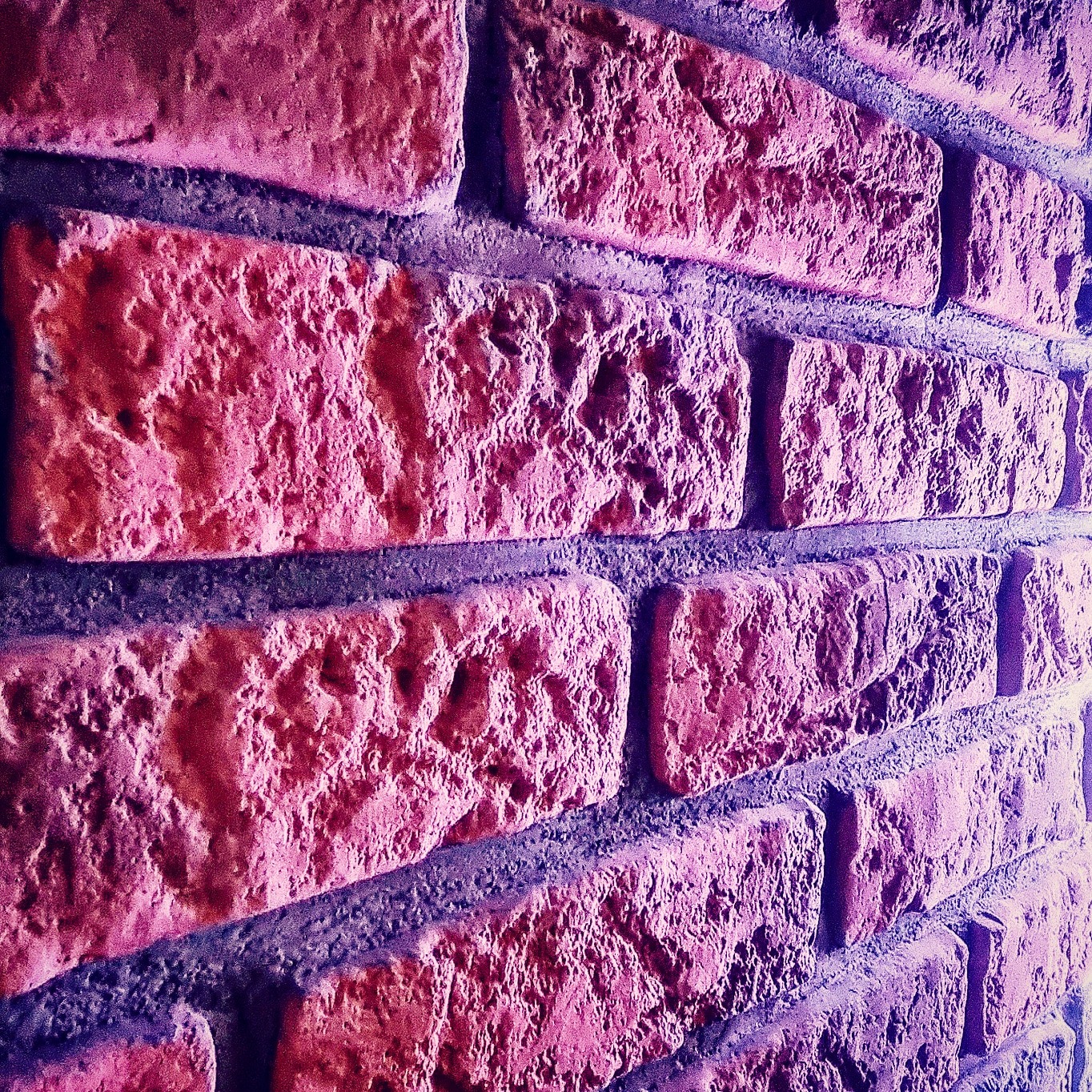 Teksturowana ściana z czerwonej cegły, ułożona z przesunięciem, z wyraźnie zaznaczonymi spoinami, oświetlona z boku, tworząca gradient kolorów.