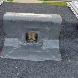 Uszczelnienie kominka wentylacyjnego na dachu pokrytym papą, z widocznymi elementami mocującymi instalację solarną.