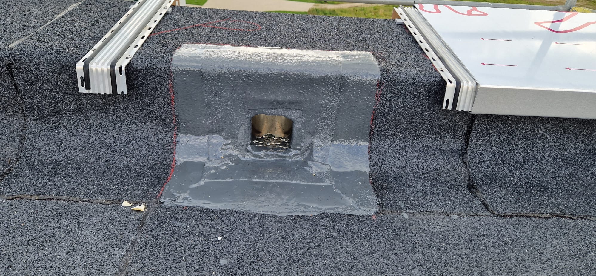 Uszczelnienie kominka wentylacyjnego na dachu pokrytym papą, z widocznymi elementami mocującymi instalację solarną.