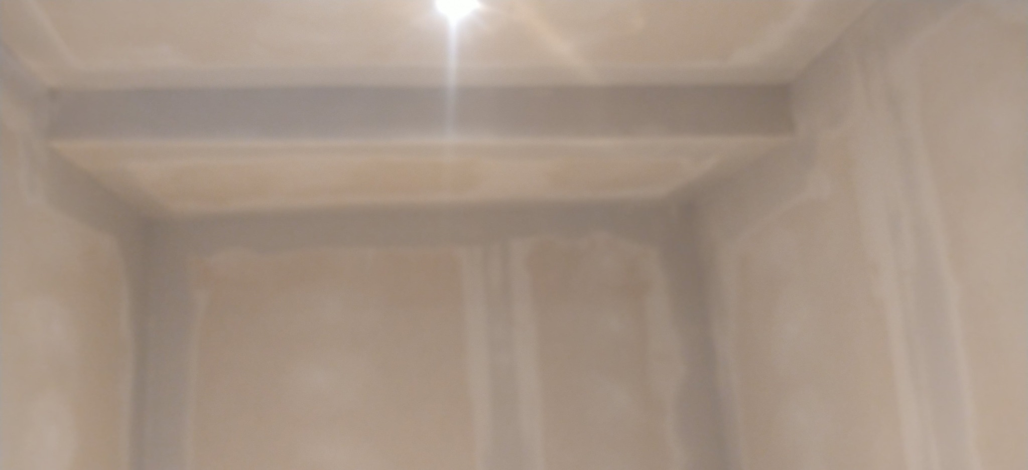 Wnętrze pokoju w trakcie wykańczania, ściany pokryte warstwą gładzi, przygotowane do dalszych prac. Widoczne łączenia płyt kartonowo-gipsowych.