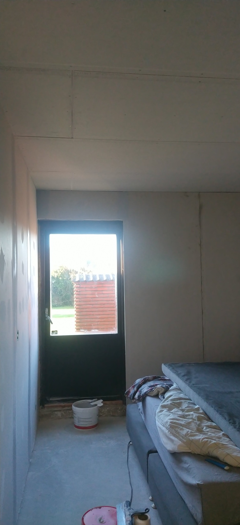 Wnętrze w trakcie prac wykończeniowych: ściany przygotowane pod malowanie, widoczna płyta karton gips na suficie, wiadro z farbą, szpachelka.