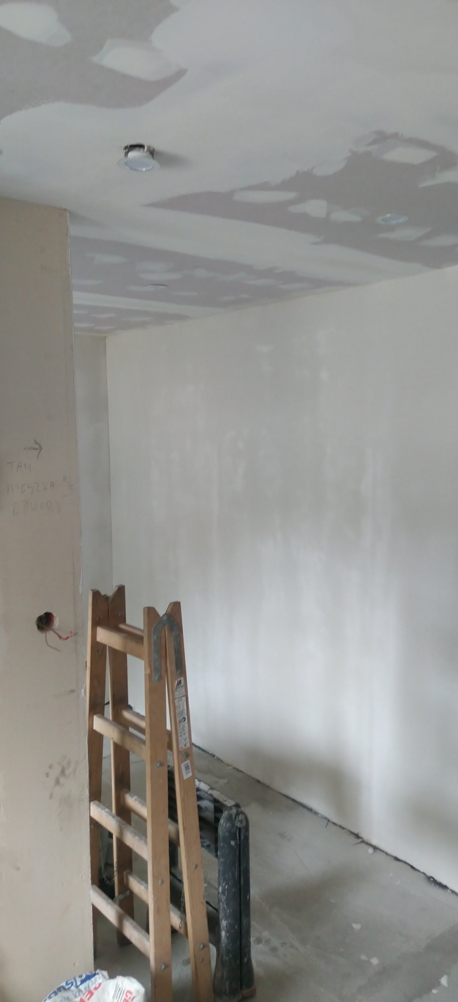 Wnętrze w trakcie prac: ściany po szpachlowaniu, sufit z widocznymi punktami świetlnymi, drabina oparta o ścianę, przygotowania do dalszych prac wykończeniowych.