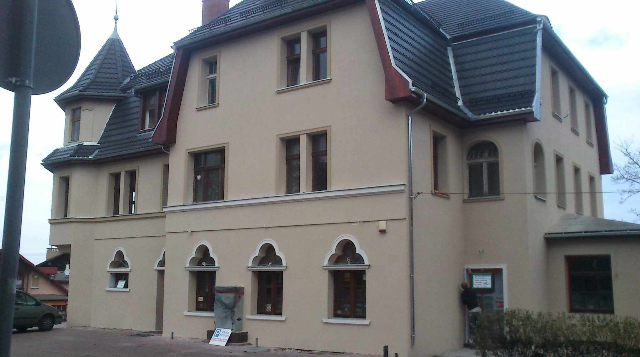 Odnowiona elewacja kamienicy z beżową fasadą, ciemnym dachem i charakterystycznymi oknami w stylu gotyckim. Widoczne detale architektoniczne i świeżo pomalowana ściana.
