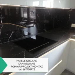 Część blatu kuchennego z czarnego marmuru z białymi żyłami, z wbudowaną płytą indukcyjną i zlewozmywakiem, oświetlona listwą LED pod szafkami wiszącymi.