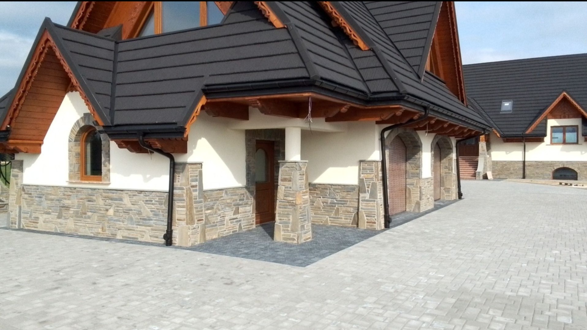Dom w stylu zakopiańskim z elewacją z kamienia naturalnego i brukowanym podjazdem z szarej kostki.
