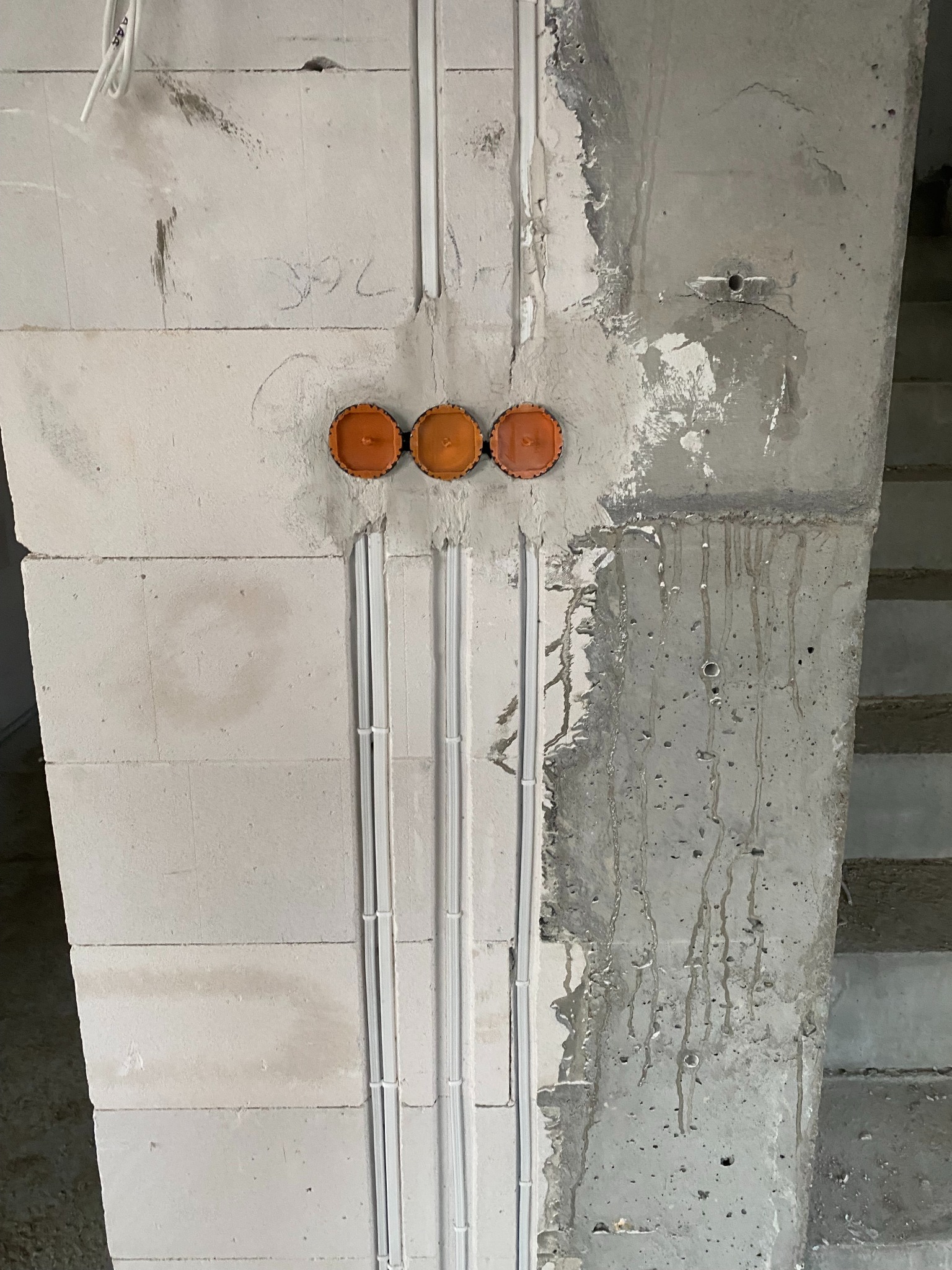 Surowy mur z trzema pomarańczowymi puszkami elektrycznymi i białymi peszlami w ścianie, widoczne ślady zaprawy, Sulimów.