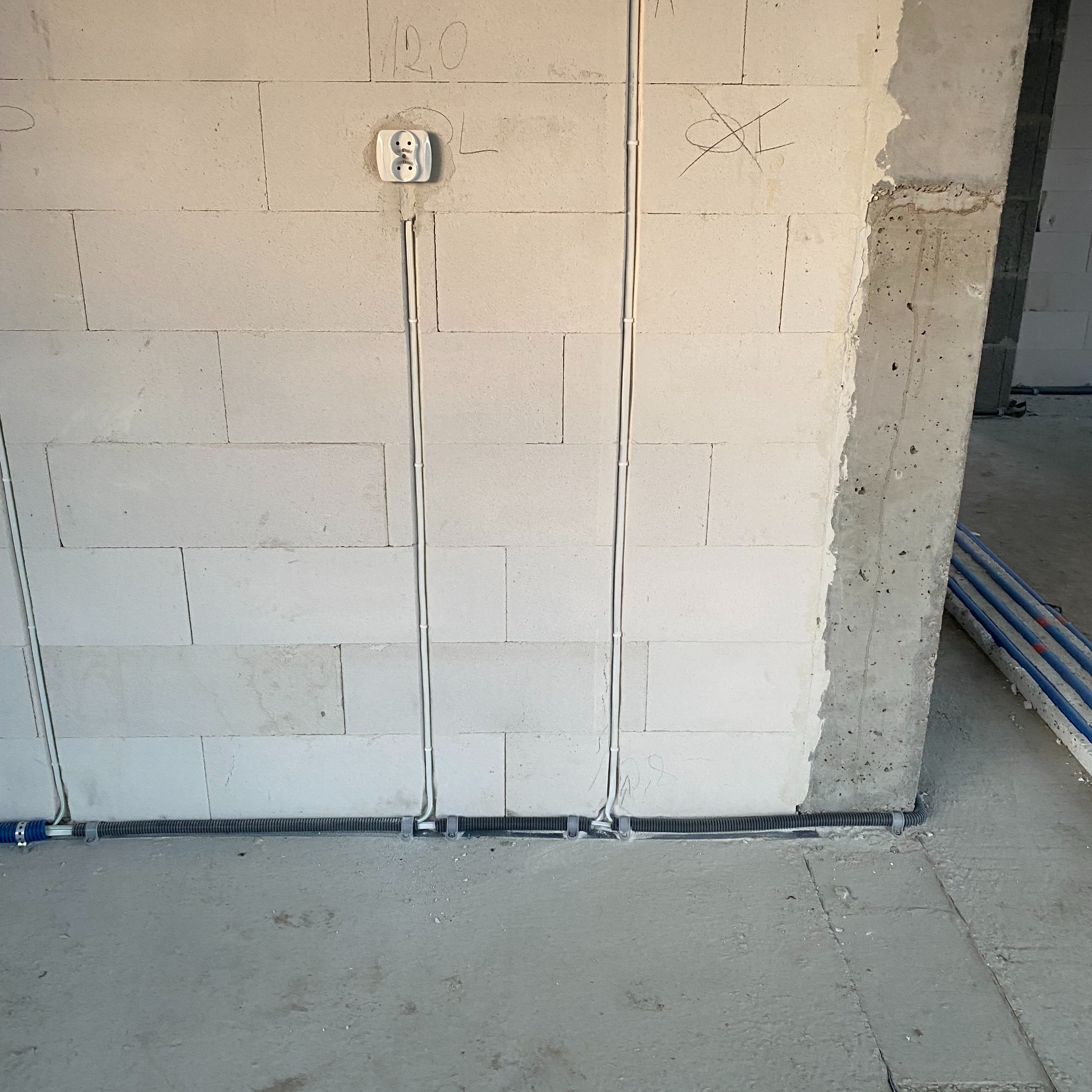 Świeżo położone przewody elektryczne w białych rurkach i czarnych peszlach na ścianie z bloczków betonowych w surowym stanie.