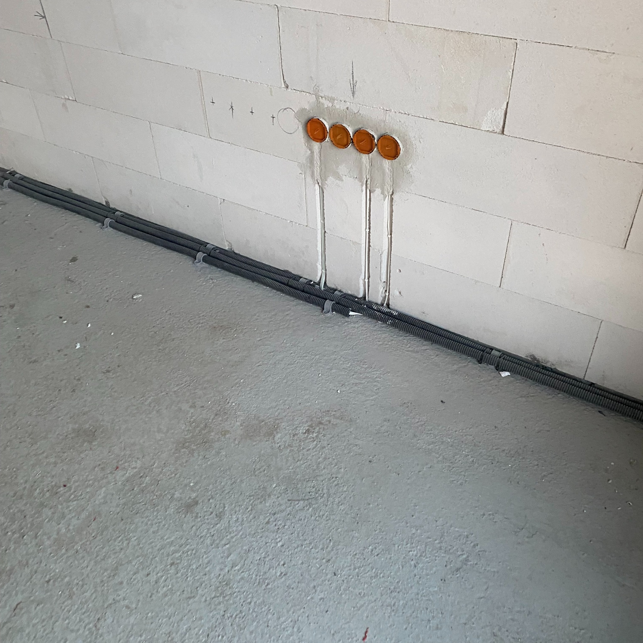 Ściana z betonu komórkowego z przygotowanymi otworami na puszki elektryczne i ułożonymi wzdłuż ściany rurami karbowanymi, zabezpieczonymi uchwytami.