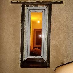 Elephant Bud Sp. Z o. O - Surowy montaż okna z pianką uszczelniającą, widoczna struktura ściany i światło z wnętrza mieszkania.