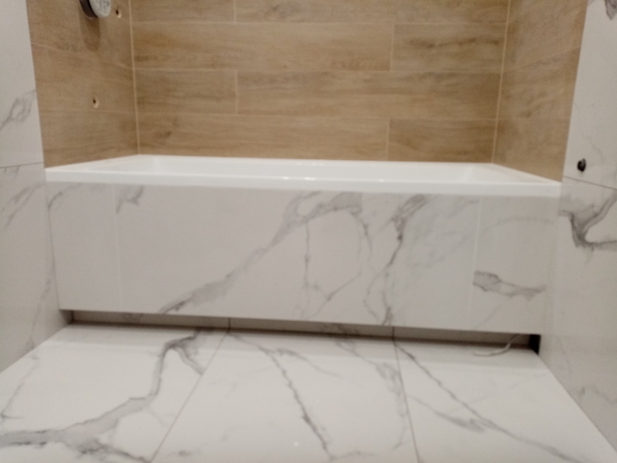 Nowoczesna wanna obudowana płytami imitującymi marmur, z beżowymi płytkami imitującymi drewno na ścianie, widok z dołu, ukazujący wykończenie podłogi również w marmurze.