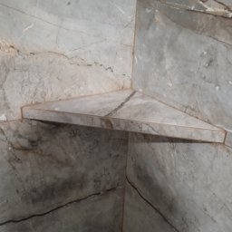 DEKOR M.O. - Narożna, trójkątna półka wyłożona marmurowymi płytkami w łazience, dopasowana do okładziny ściennej.