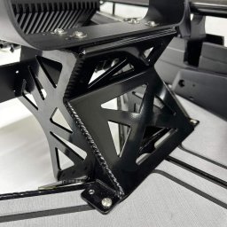 PANFAB Wiktor Drążek - Czarny, metalowy wspornik z wyciętymi trójkątami, przymocowany śrubami do szarej powierzchni z czarnymi paskami, widoczne spawy i logo producenta 'ARMIN'.