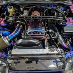 Szczegółowe ujęcie silnika samochodowego po tuningu z widocznym aluminiowym radiatorem Mishimoto, rurami w kolorze tytanu i karbonowymi elementami obudowy.