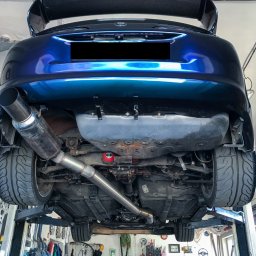 PANFAB Wiktor Drążek - Niebieski samochód sportowy na podnośniku w warsztacie, widok od spodu, z widocznym układem wydechowym ze stali nierdzewnej i karbonowym spojlerem.