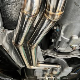 PANFAB Wiktor Drążek - Widok od spodu na spawany, polerowany układ wydechowy z rur nierdzewnych, zamontowany w samochodzie, z widocznymi spawami i elementami mocującymi.