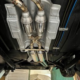 PANFAB Wiktor Drążek - Widok od dołu na podwozie samochodu z zamontowanym, nowym układem wydechowym ze stali nierdzewnej. Widoczne spawane łączenia rur wydechowych oraz osłona termiczna z perforowanej blachy.