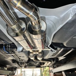 PANFAB Wiktor Drążek - Widok od spodu na zamontowany, polerowany, nierdzewny układ wydechowy z podwójnymi końcówkami w samochodzie na podnośniku.