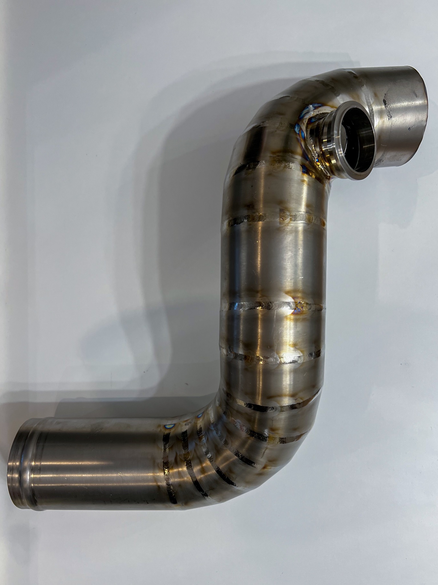 Precyzyjnie pospawany, nierdzewny rurociąg o zakrzywionym kształcie, z widocznymi śladami spawania TIG, leżący na białym tle.