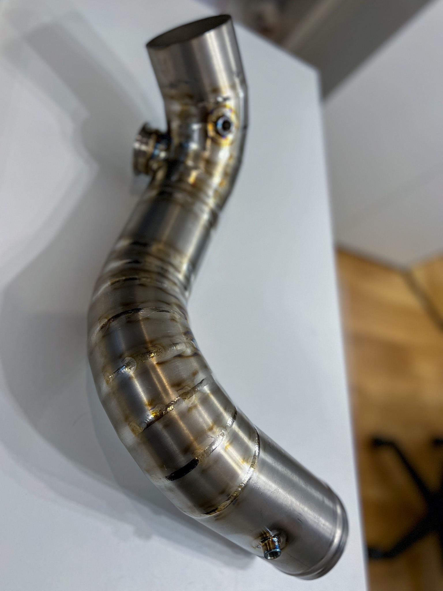 Precyzyjnie spawany, zakrzywiony element rury ze stali nierdzewnej z widocznymi śladami spawania, prezentowany na białym tle.